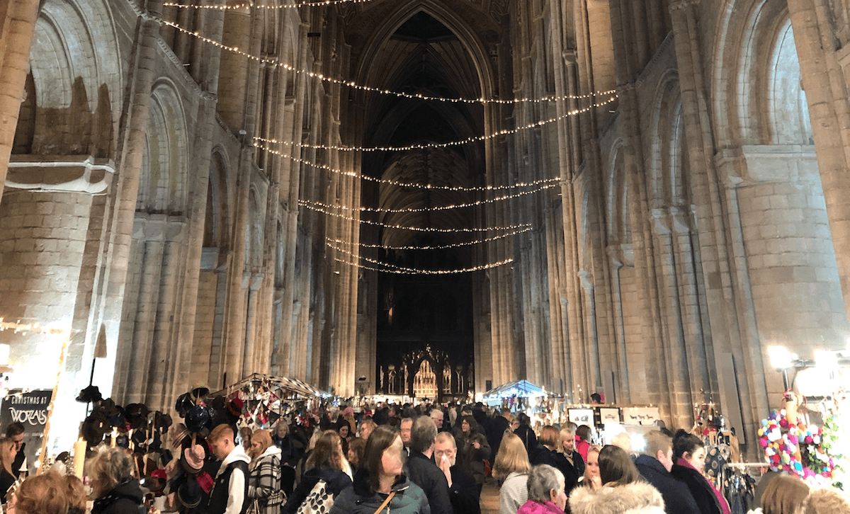 Things to do in East Cambs in Autumn -Ely Cathedral Christmas Gift & Food Fair. Market goers inside Cathedral walking past stalls